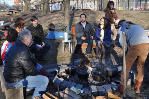 A group of adult visitors to the Wyckoff farmhouse gathers around the outdoor hearth