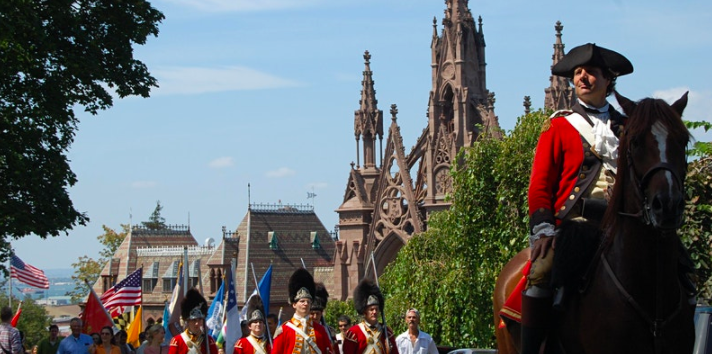 Reenactors in Revolutionary War dress parading down a path at Green-Wood Cemetery.